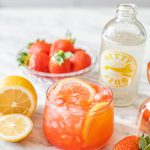 a strawberry mocktail with lemon wedge and bowl of strawberries