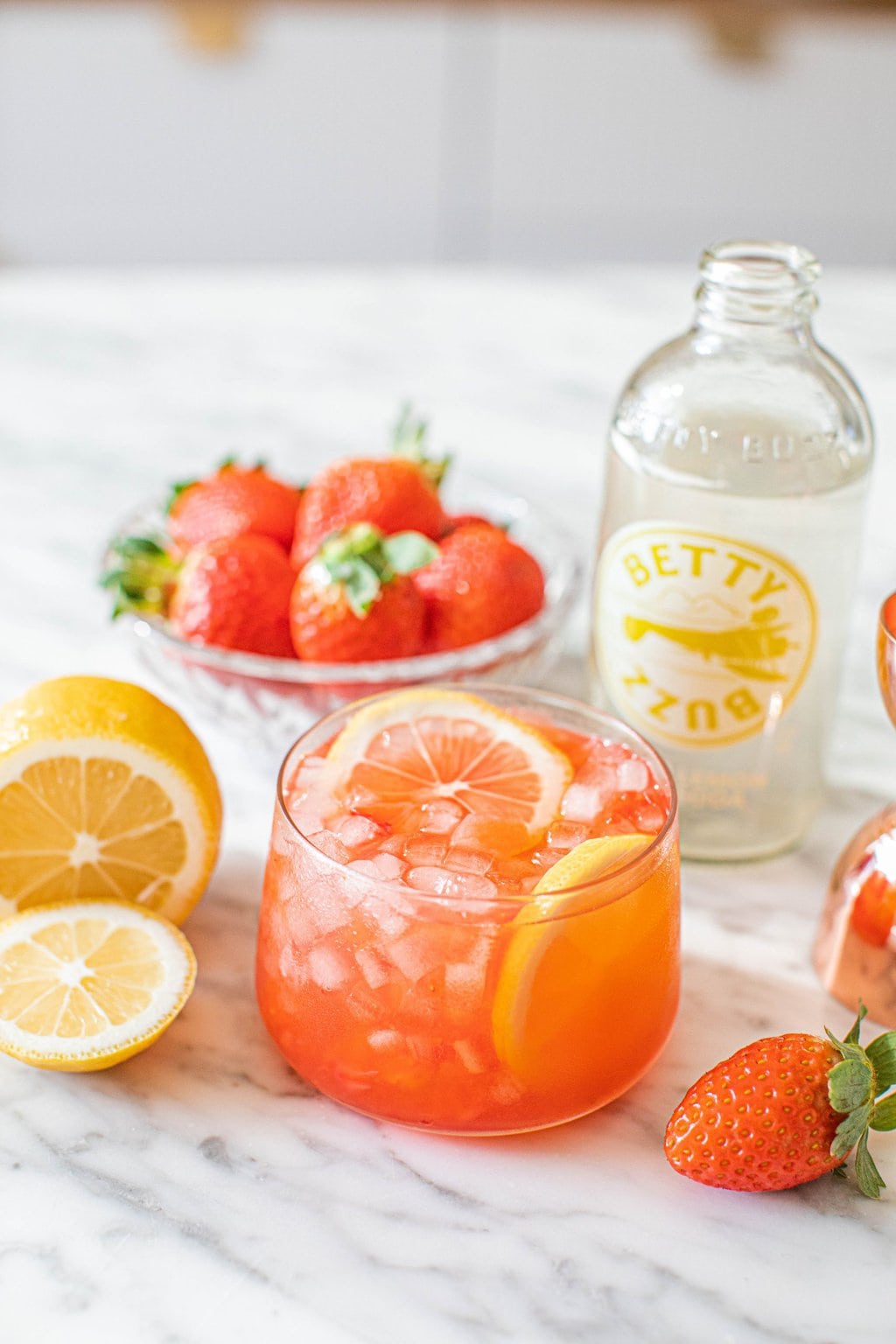 a strawberry mocktail with lemon wedge and bowl of strawberries