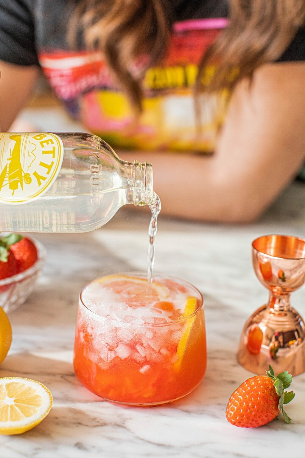 pouring lemon soda into a strawberry mocktail glass 