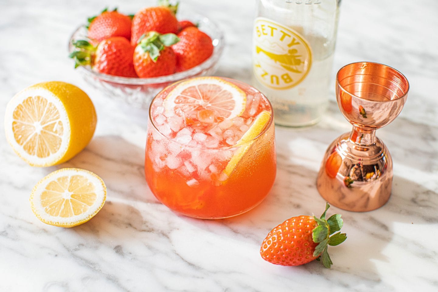 lemon and lemon slice, bowl of strawberries, strawberry drink, lemon lime soda and a copper jigger