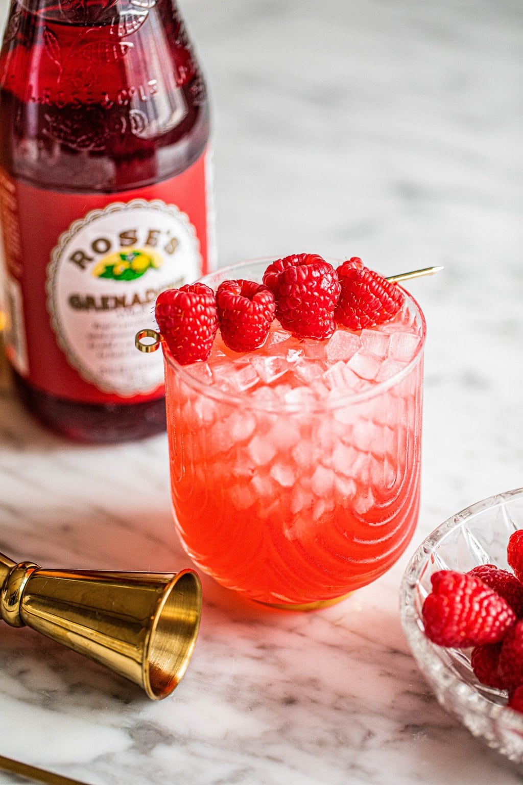 champagne with vodka cocktail in glass garnished with raspberries on gold skewer