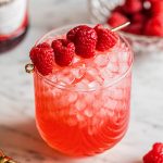 vodka champagne cocktail in glass garnished with raspberries on gold skewer