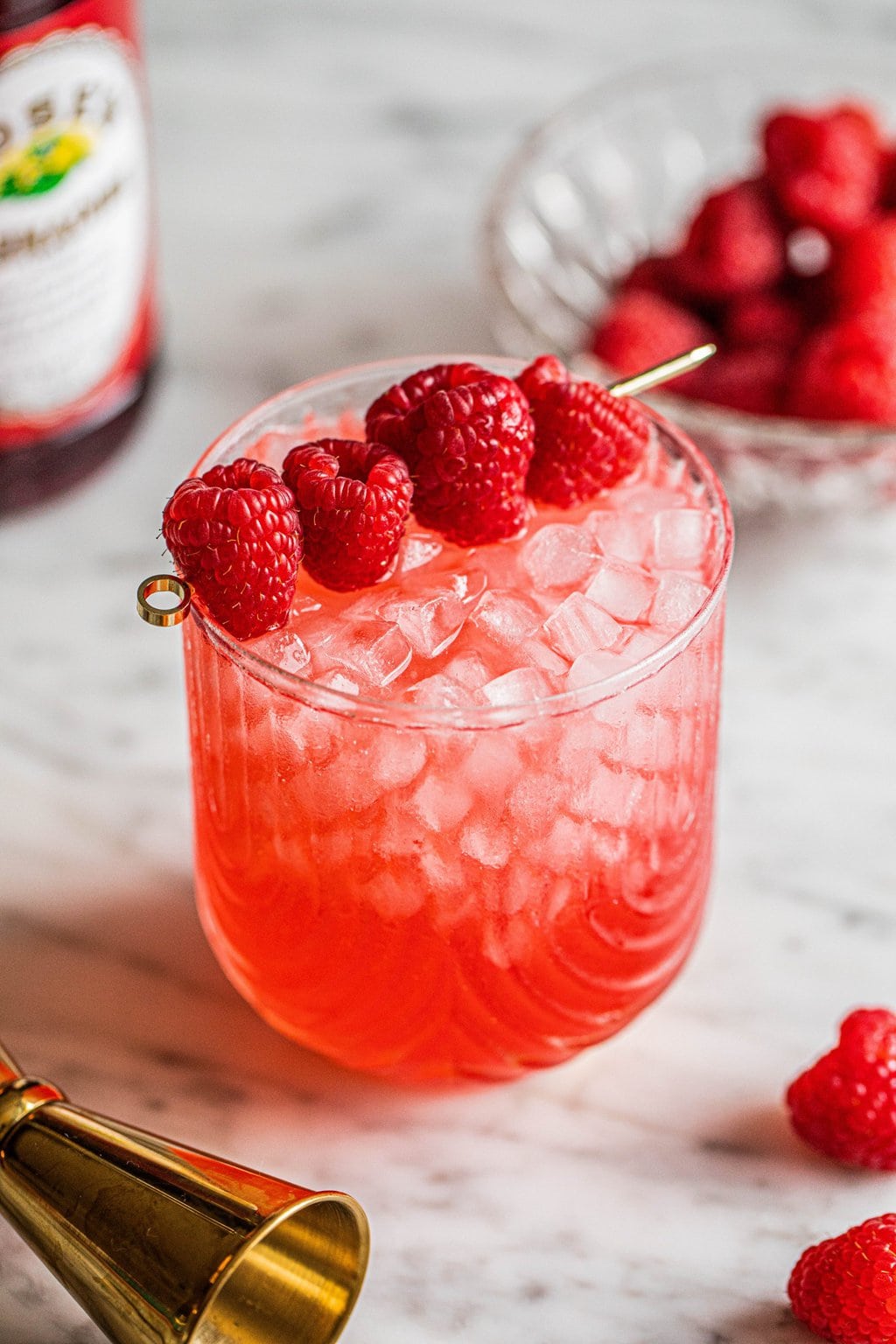 vodka champagne cocktail in glass garnished with raspberries on gold skewer