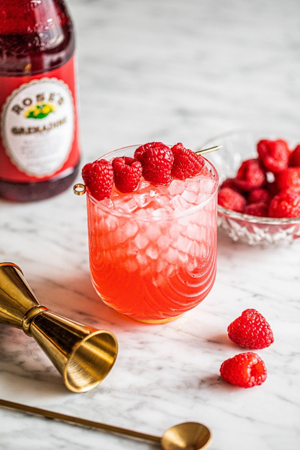 champagne with vodka cocktail in glass garnished with raspberries on gold skewer