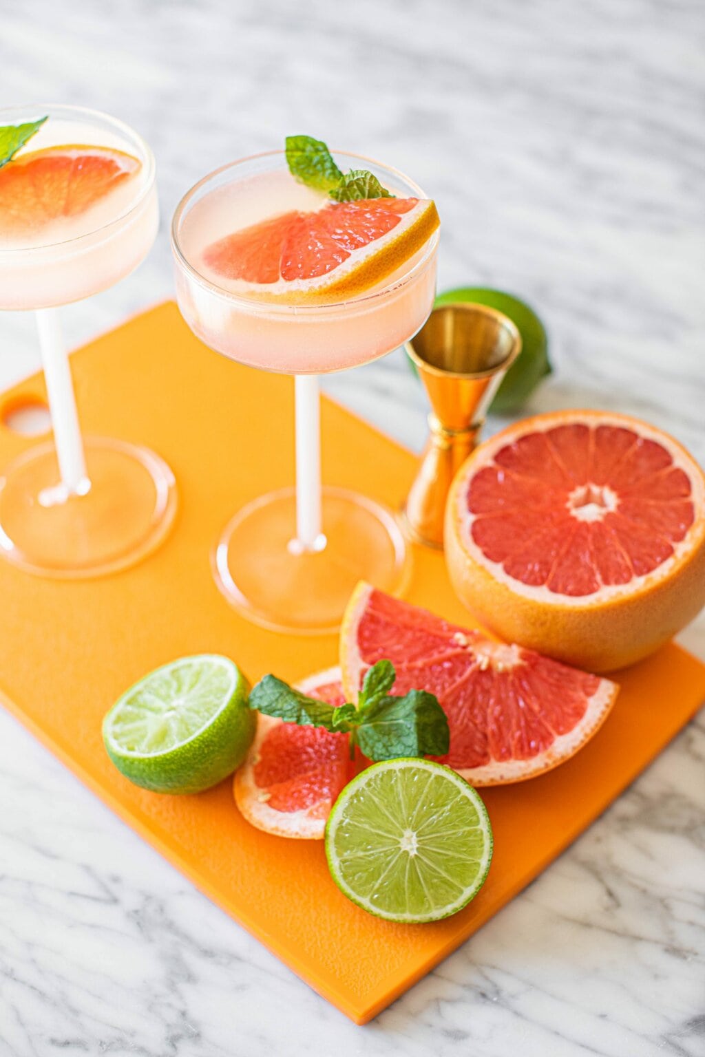 two grapefruit vodka martinis in coupe glasses on orange board