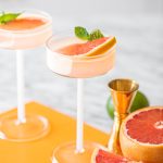 two pink grapefruit martinis in coupe glasses on orange board