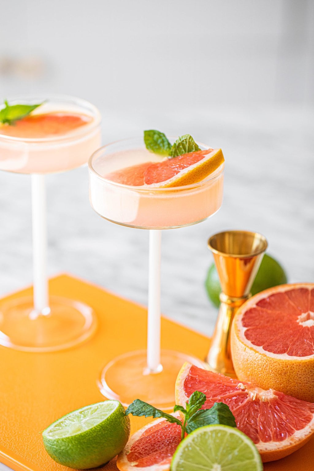 two pink grapefruit martinis in coupe glasses on orange board