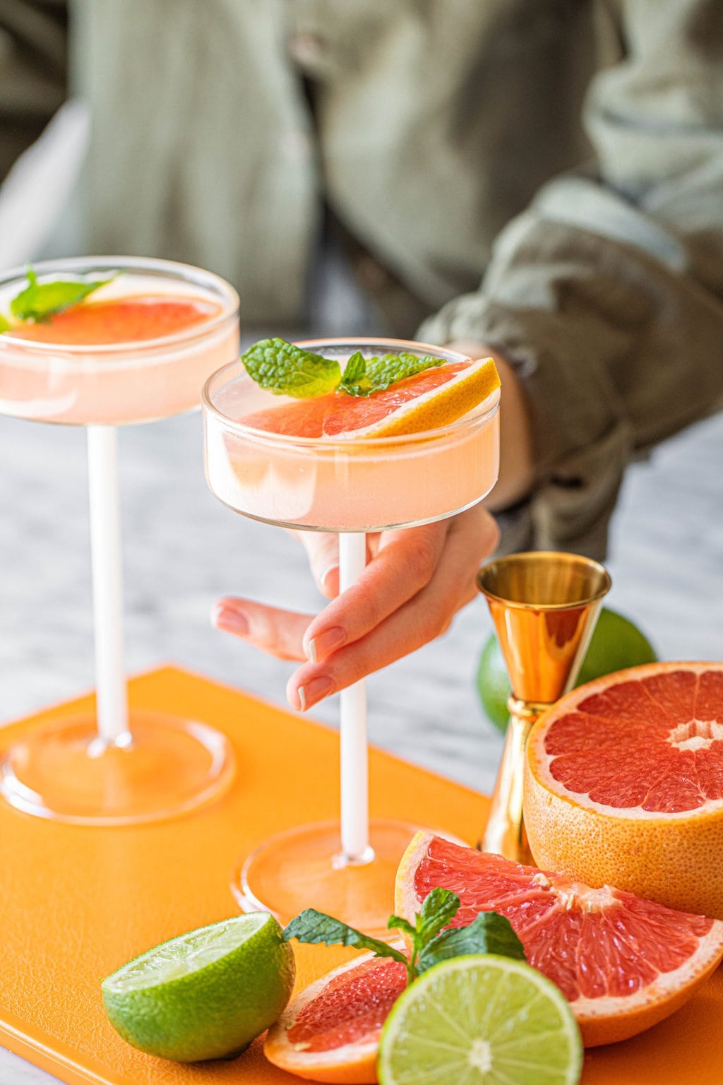 woman's hand grabbing pink grapefruit martini in coupe glass