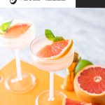 two grapefruit vodka martinis in coupe glasses on orange board