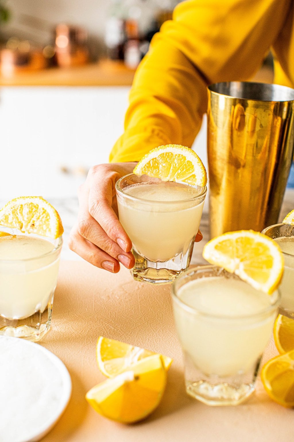 woman holding lemon drop shot in shot glass with lemon wedge