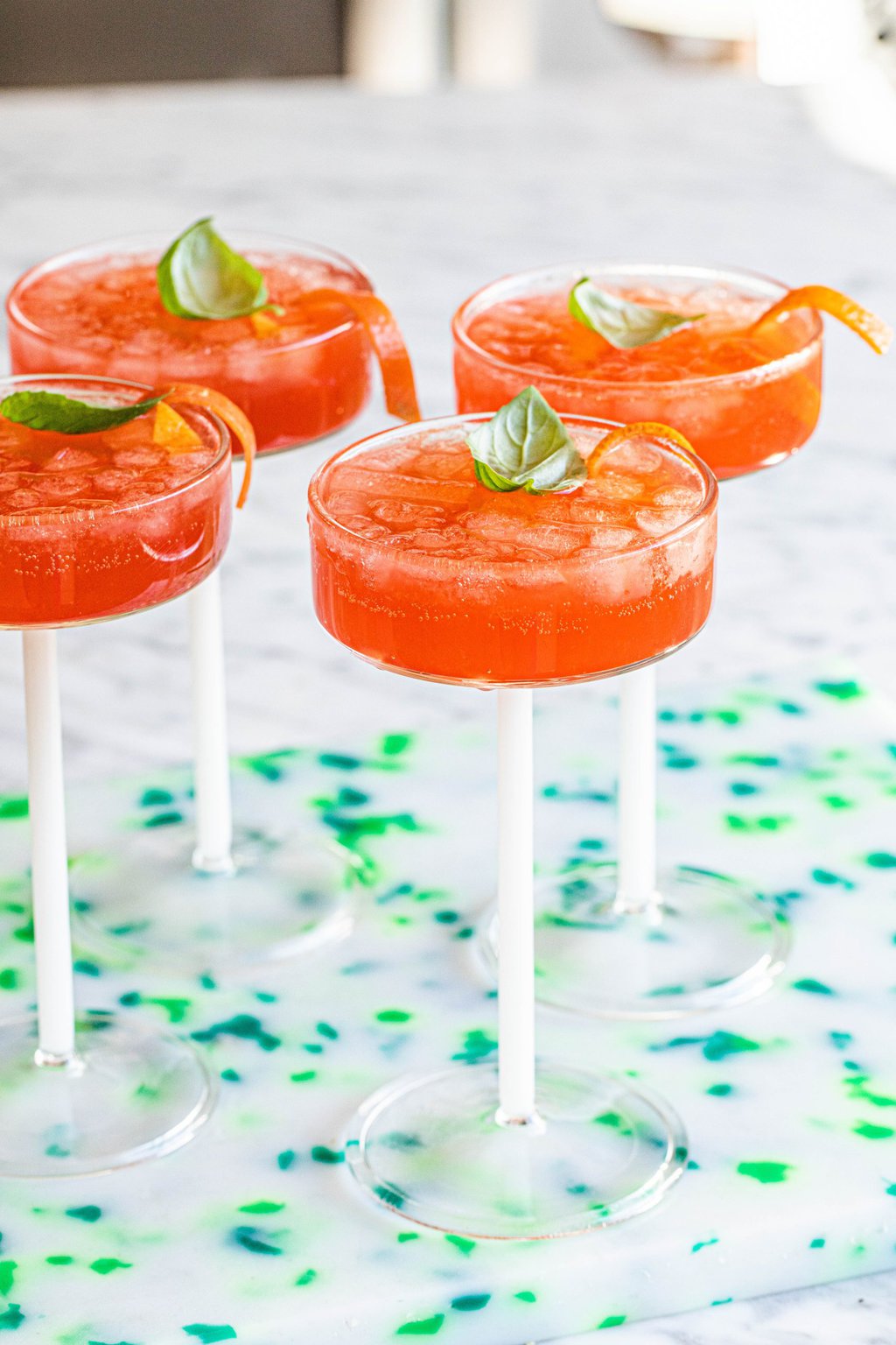 four negroni spritz cocktails in coup glass garnished with basil leaf