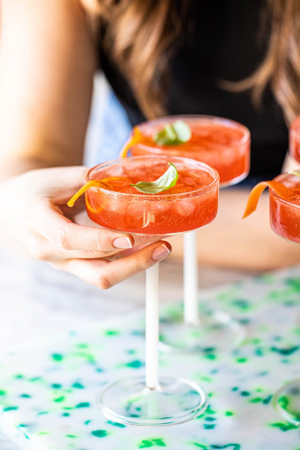 woman grabbing negroni spritzer in coupe glass