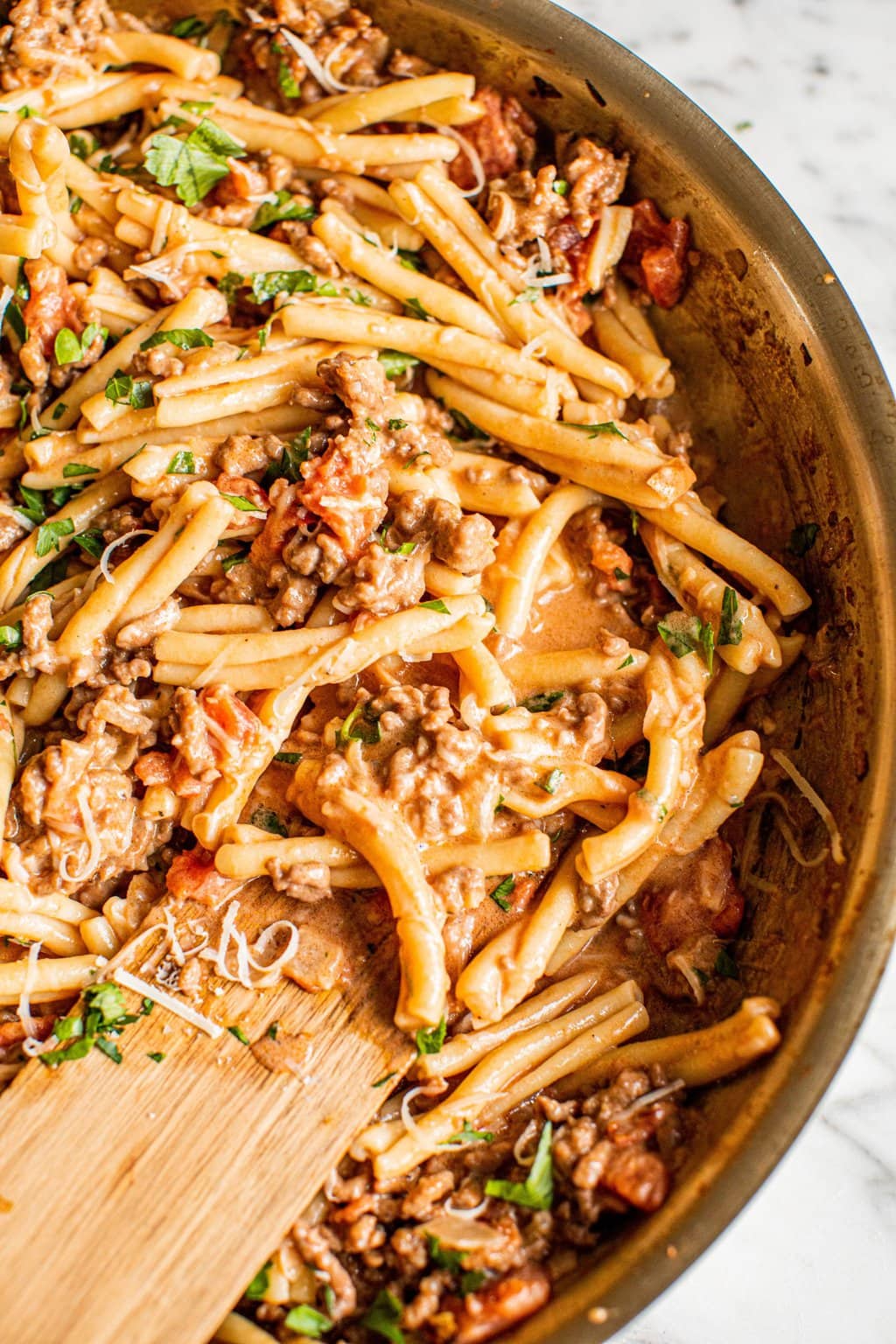 spicy sausage pasta in skillet with wooden spoon