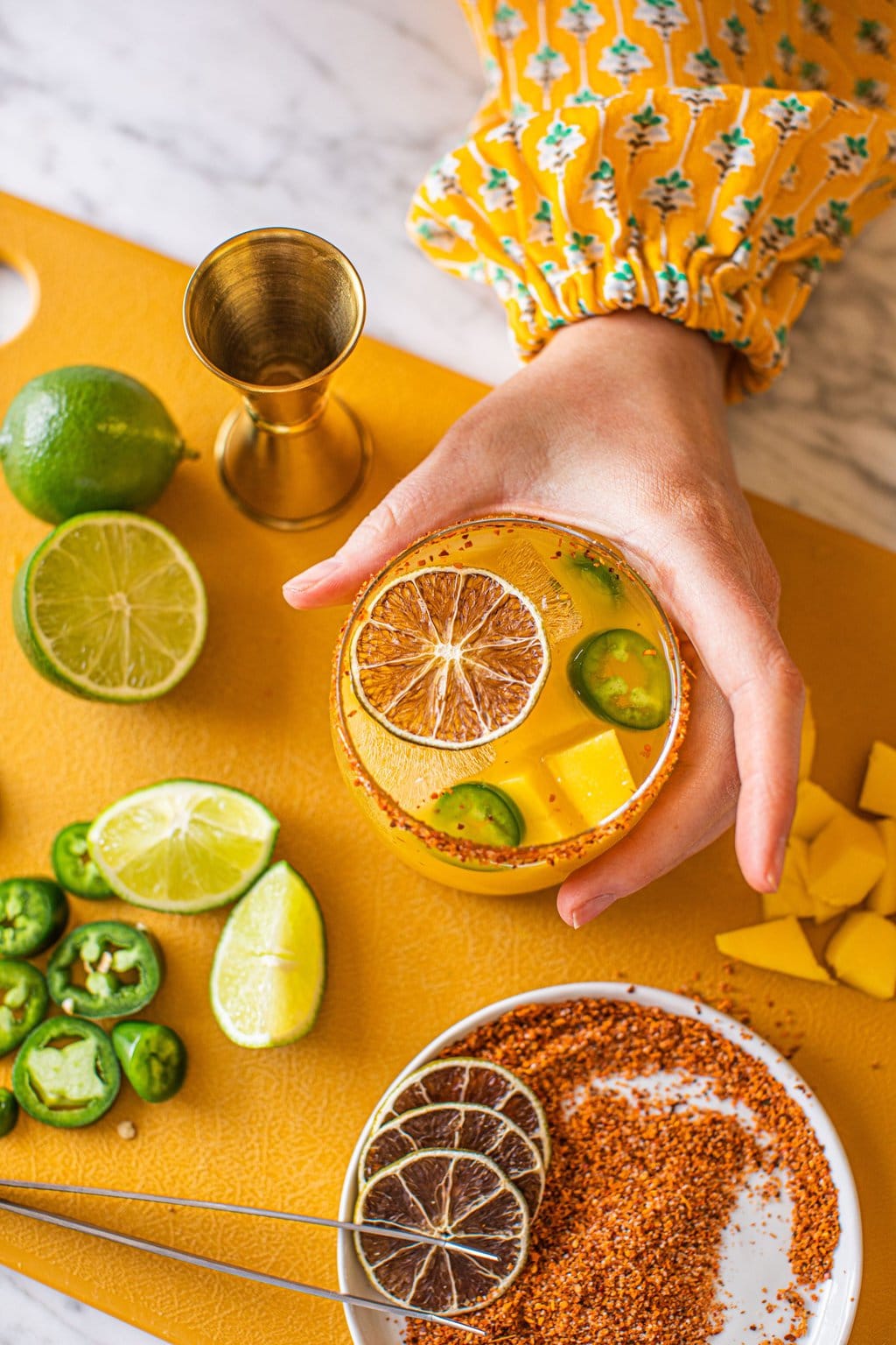 woman's hand grabbing spicy mango jalapeno margarita in low ball glass