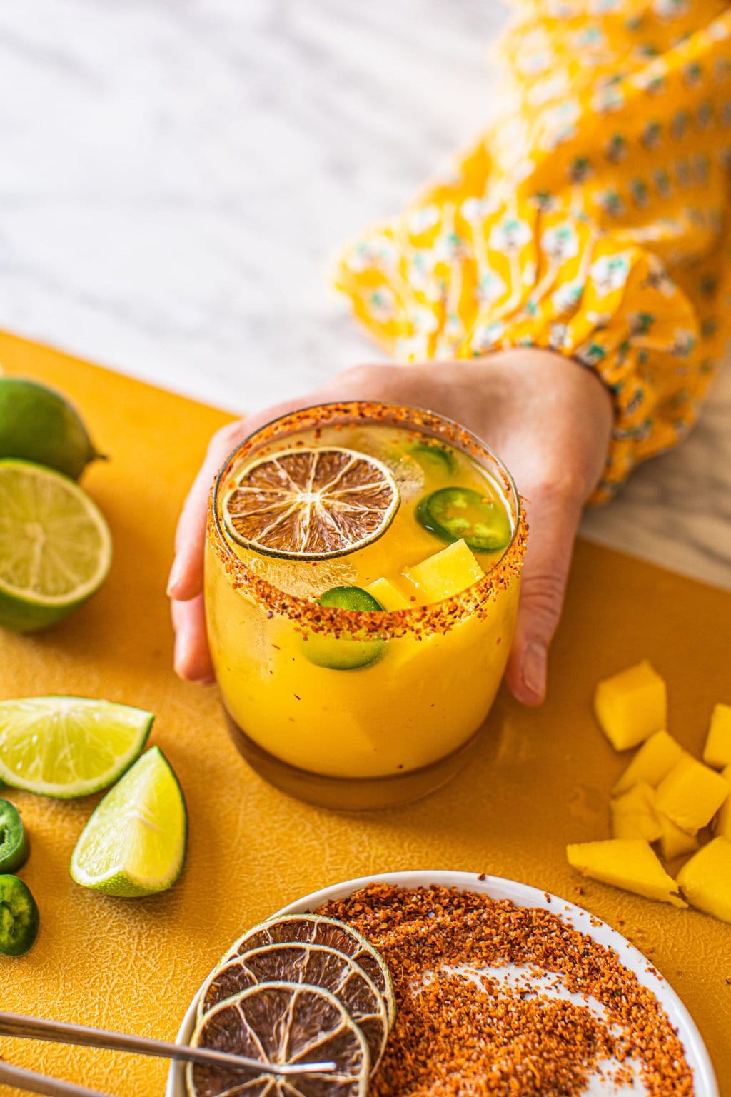 woman's hand grabbing spicy mango margarita in low ball glass