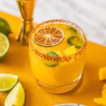 woman's hand grabbing spicy jalapeno mango margarita in low ball glass