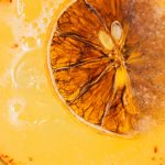 orange margarita with a slice of orange in it and tajin on the rim