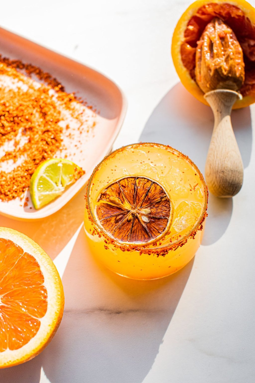 orange margarita with a slice of orange in it and tajin around the rim 