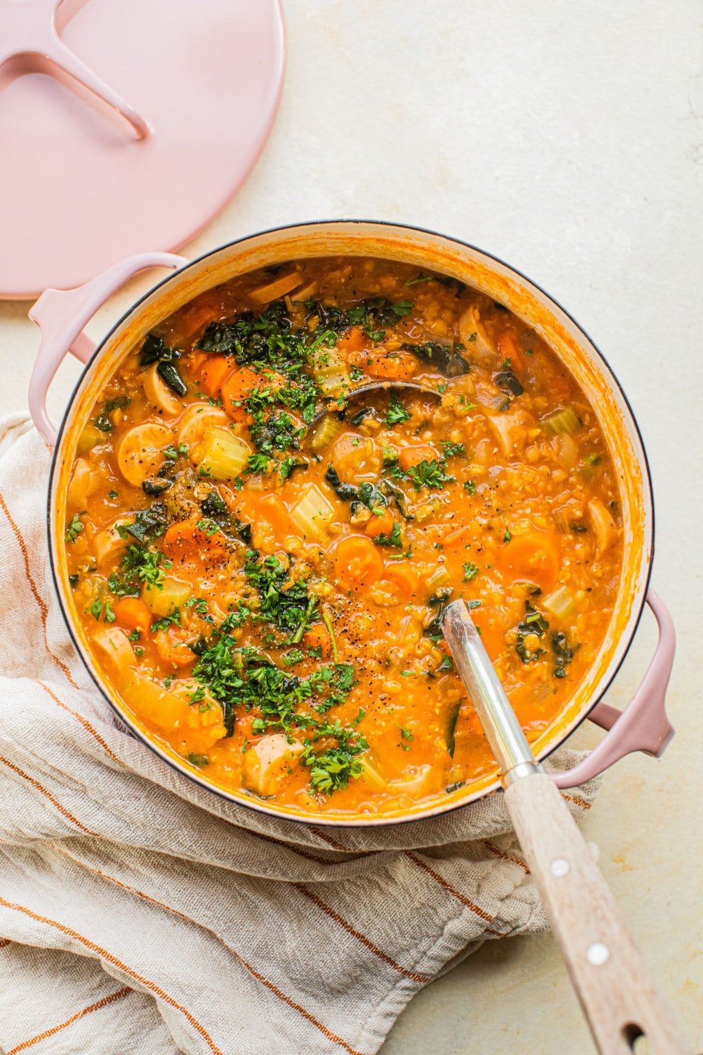 an overhead photo of lentil soup in a pink dutch oven with a lade in it