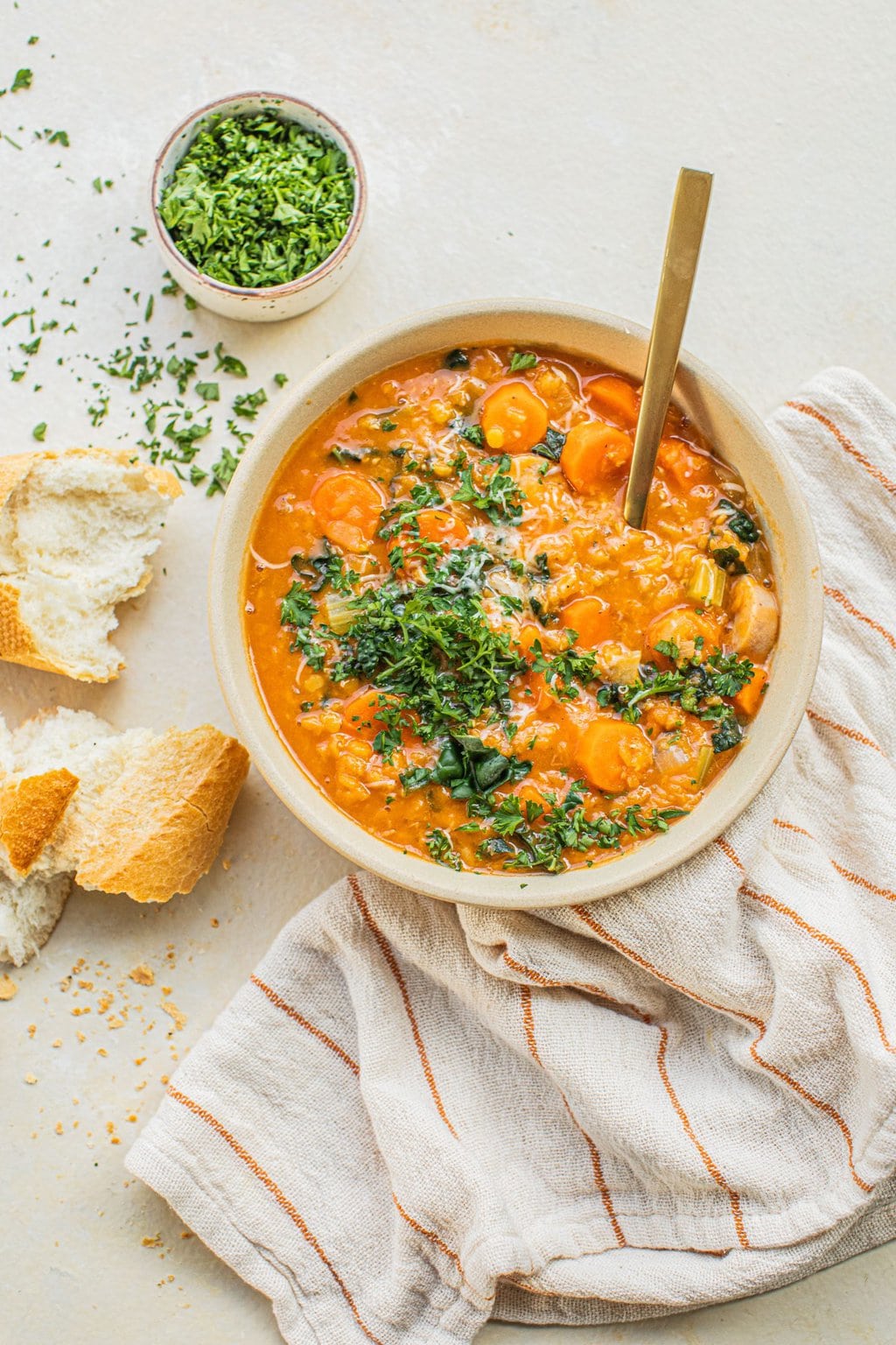 a bowl of soup with parsley on top, extra parsley in a bowl on the side, and a piece of bread to dip 