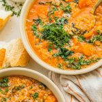 two bowls of carrot and lentil soup topped with parsley