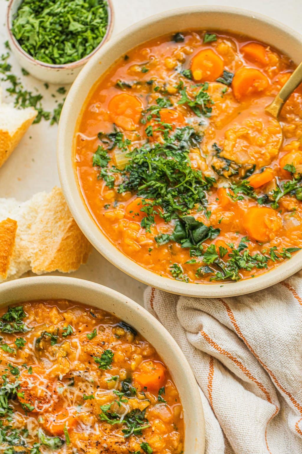 two bowls of carrot and lentil soup topped with parsley