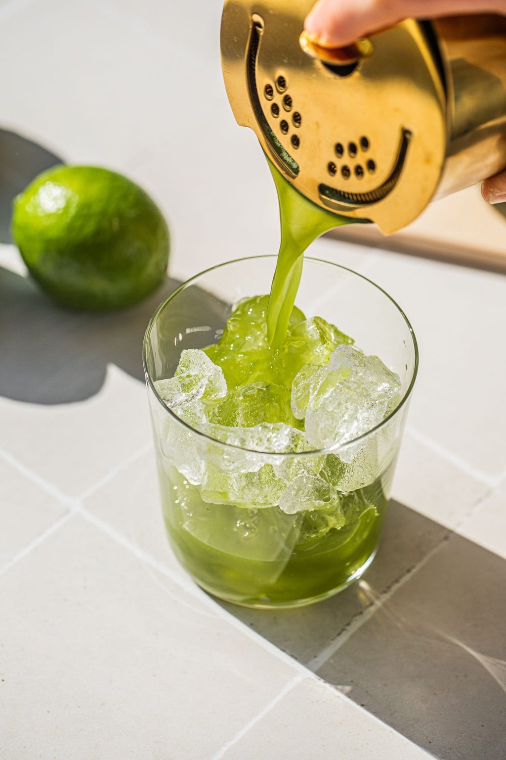 straining the matcha cocktail into an old fashioned glass over ice