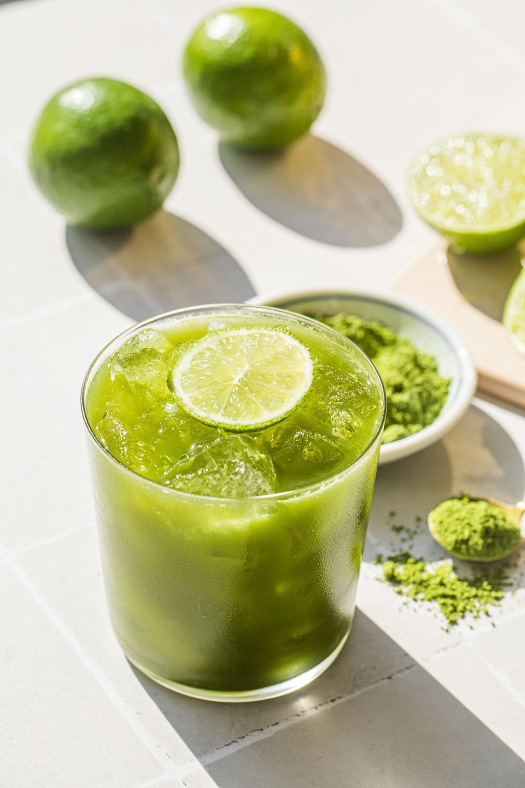 an old-fashioned glass full of a green margarita with a lime wedge on top for garnish, and match powder in the background