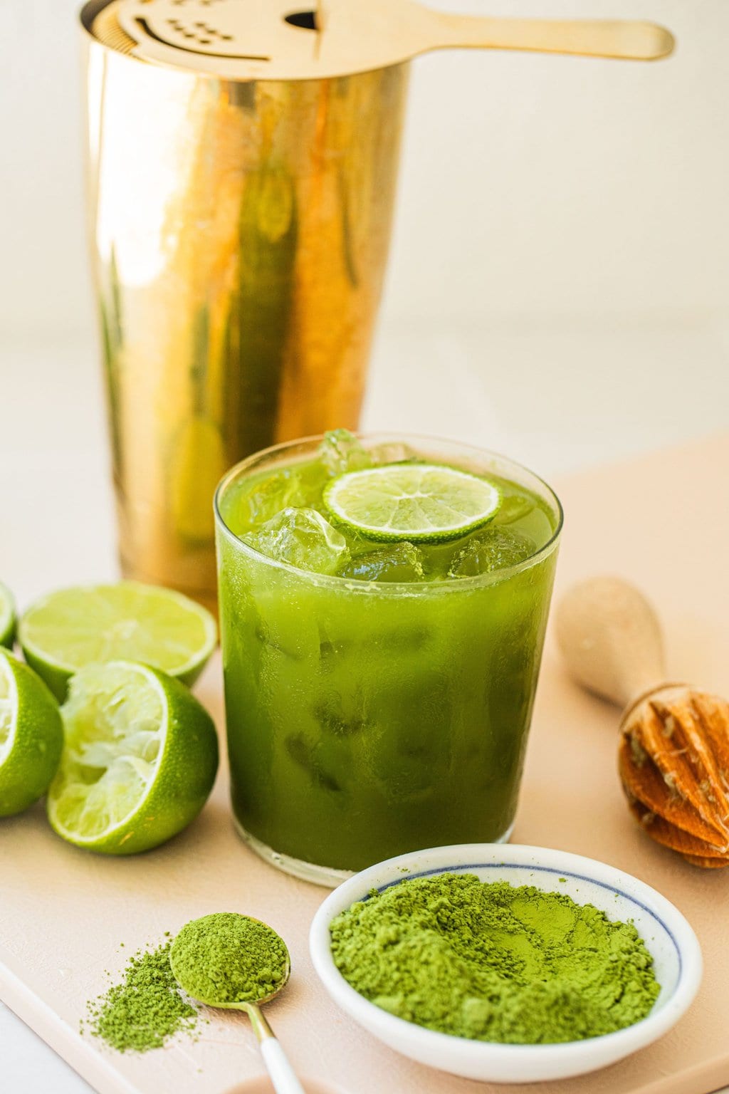 matcha margarita garnished with a slice of lime in a small glass with a gold cocktail shaker in the background