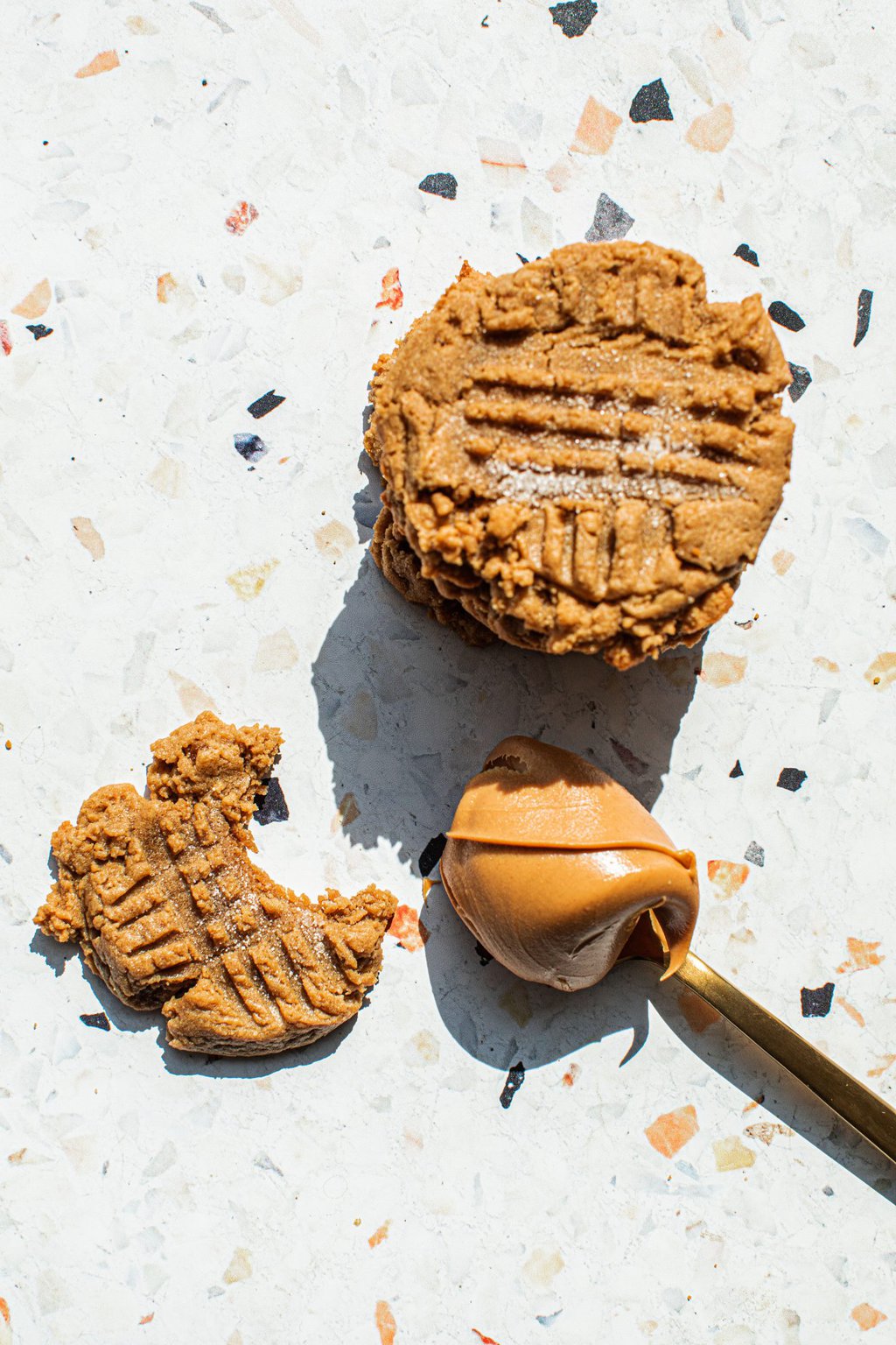 a stack of peanut butter cookies beside a lone cookie and a spoonful of peanut butter