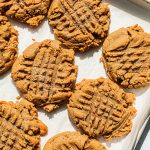 several peanut butter cookies scored in a criss cross design on a parchment lined baking sheet
