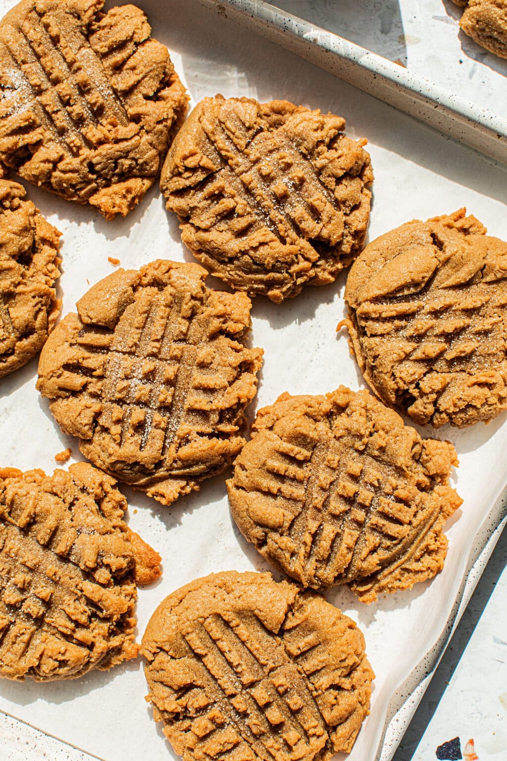 several peanut butter cookies scored in a criss cross design on a parchment lined baking sheet