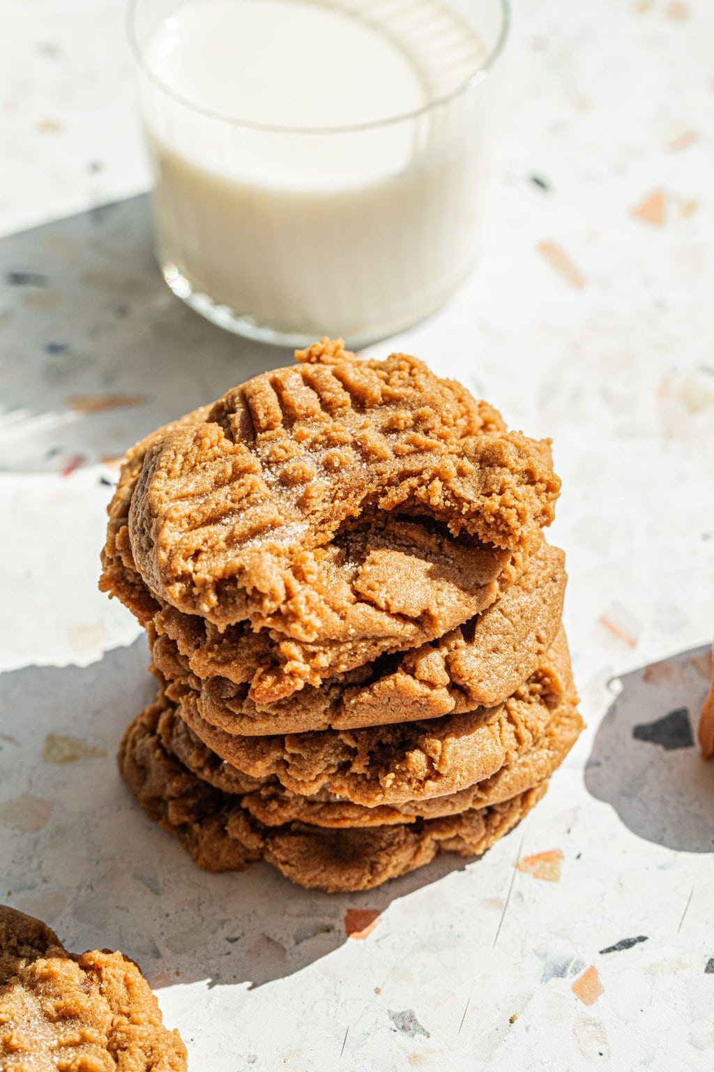 a stack of peanut butter cookies with a bite taken out of the top one and a cup of milk in the background