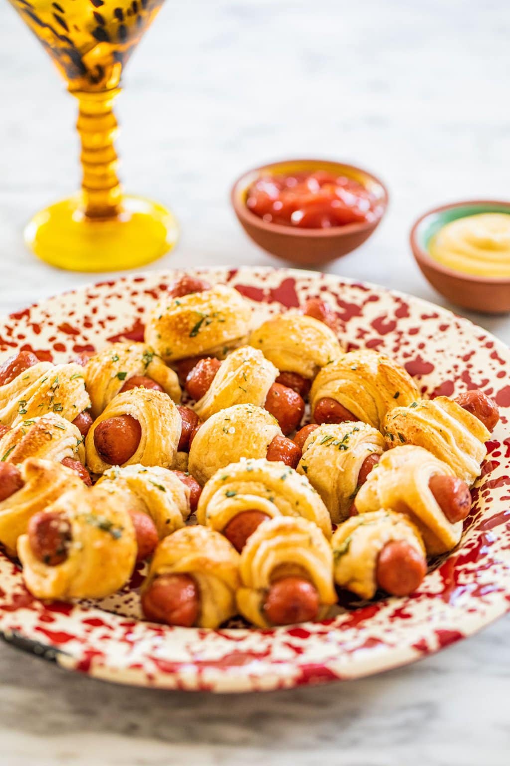 a red and white plate full of dough wrapped hot dogs with a martini and two bowls of dip in the background