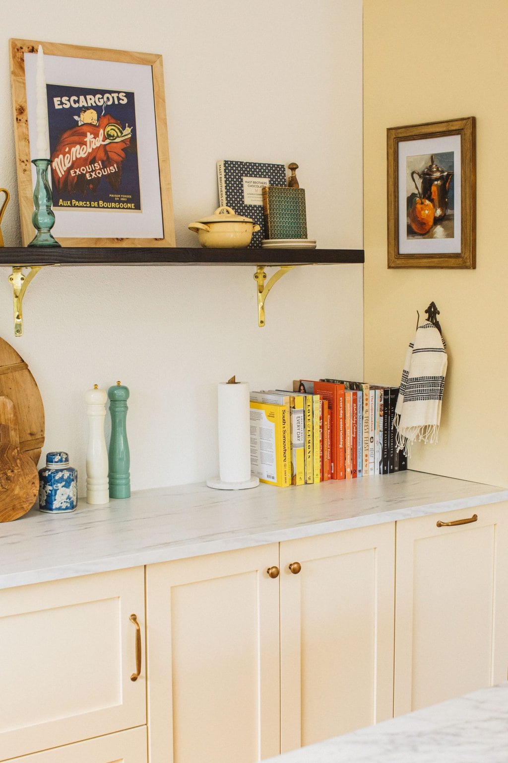 cream colored cabinets, marble counter tops, oil paintings, old french cookbooks, cookbooks and salt and pepper shaker 