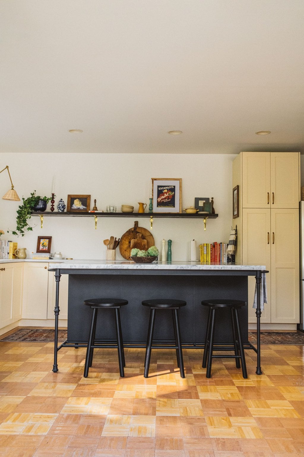 large black island with marble counter top, three small black stools and cream kitchen cabinets 