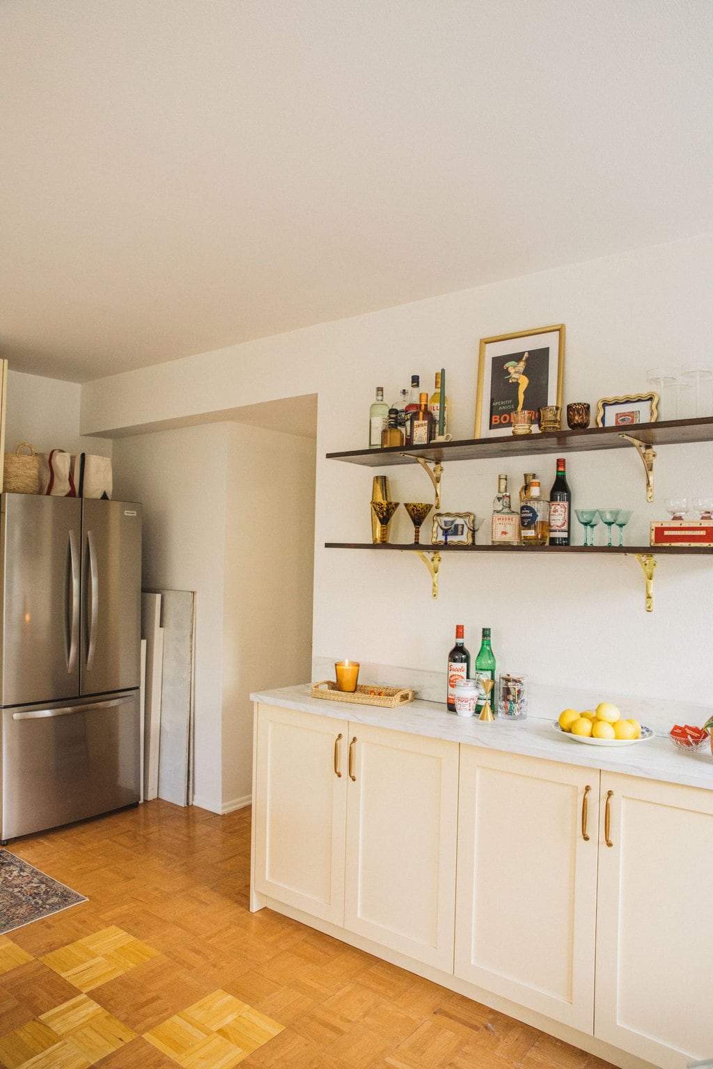 stainless steel refrigerator, open shelves with bottles of liquor and cream kitchen cabinets  