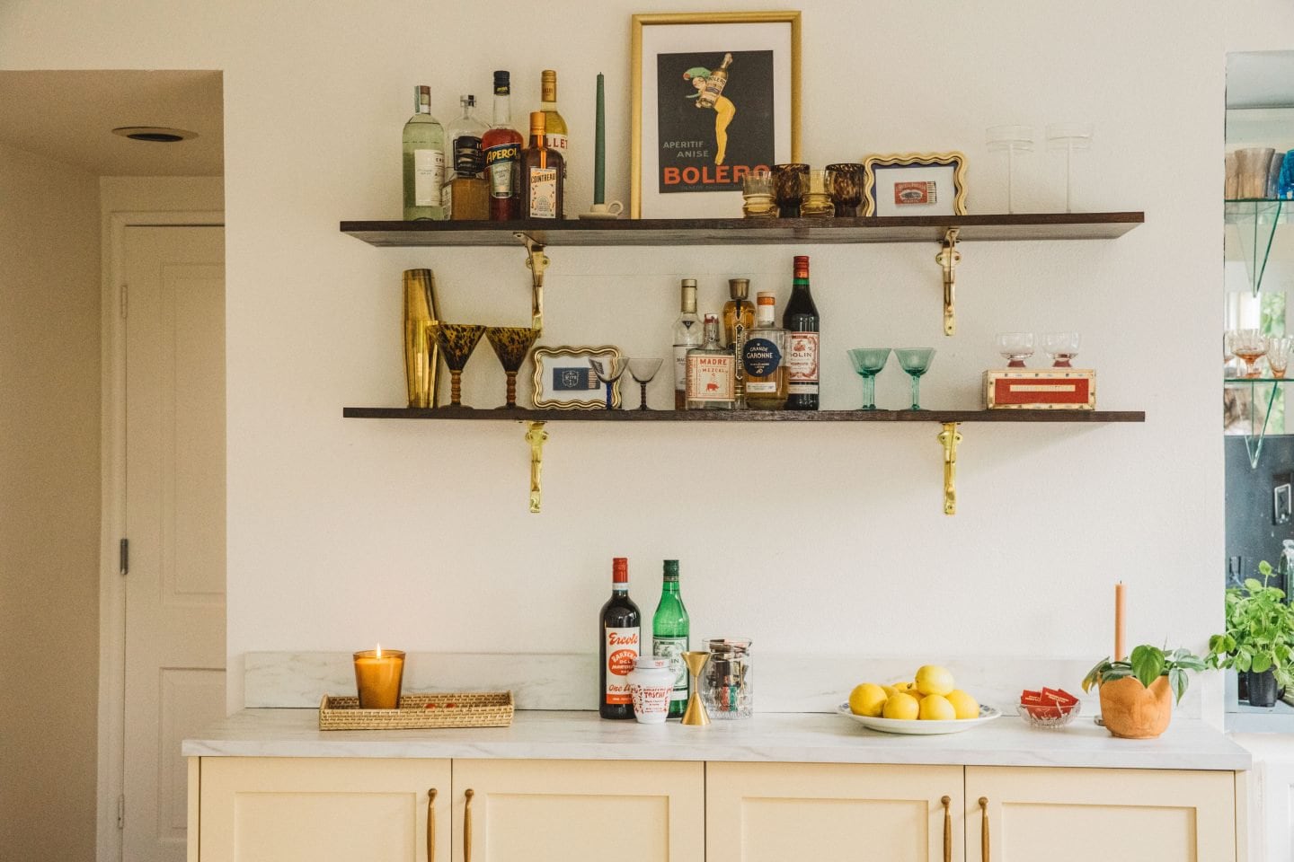 open shelving with liquor bottles, french prints and cream colored cabinets 