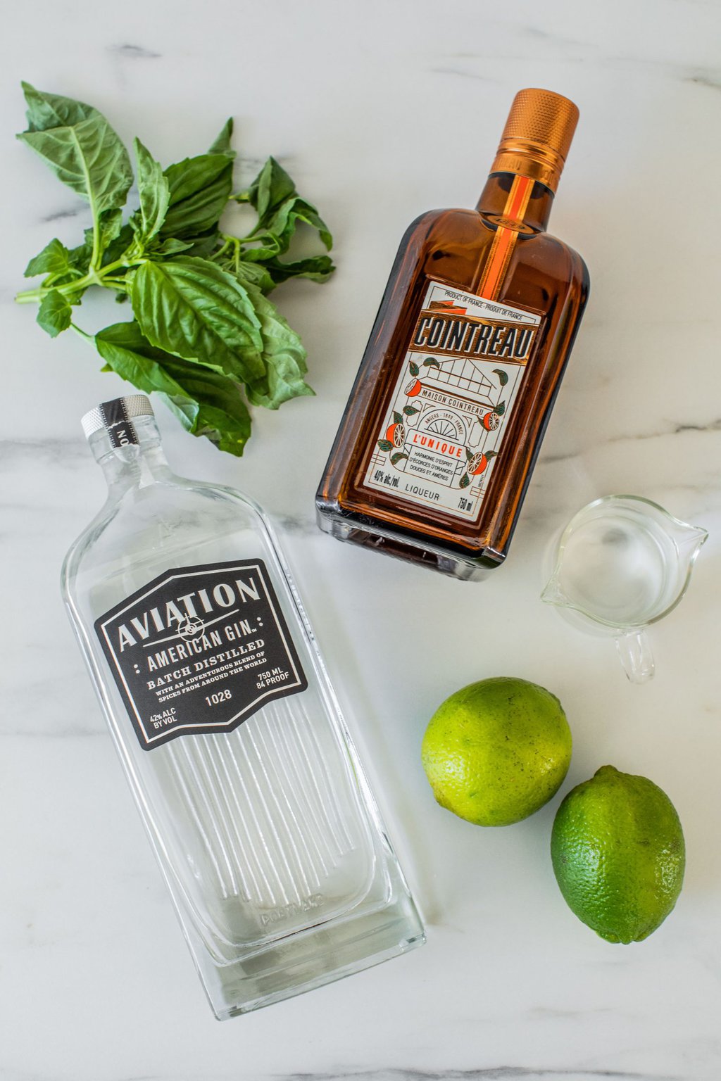 gin, basil leaves, Cointreau, lime, and simple syrup on a white marble countertop