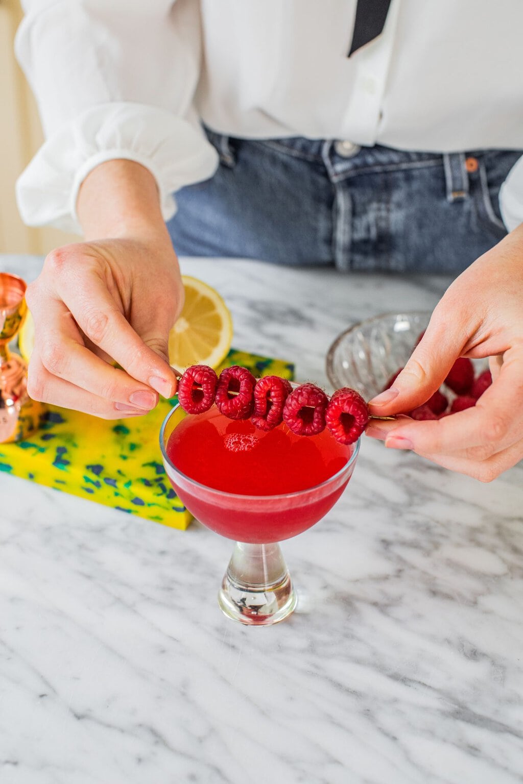 a martini made with raspberries and vodka in a glass and garnished with more raspberries on a toothpick