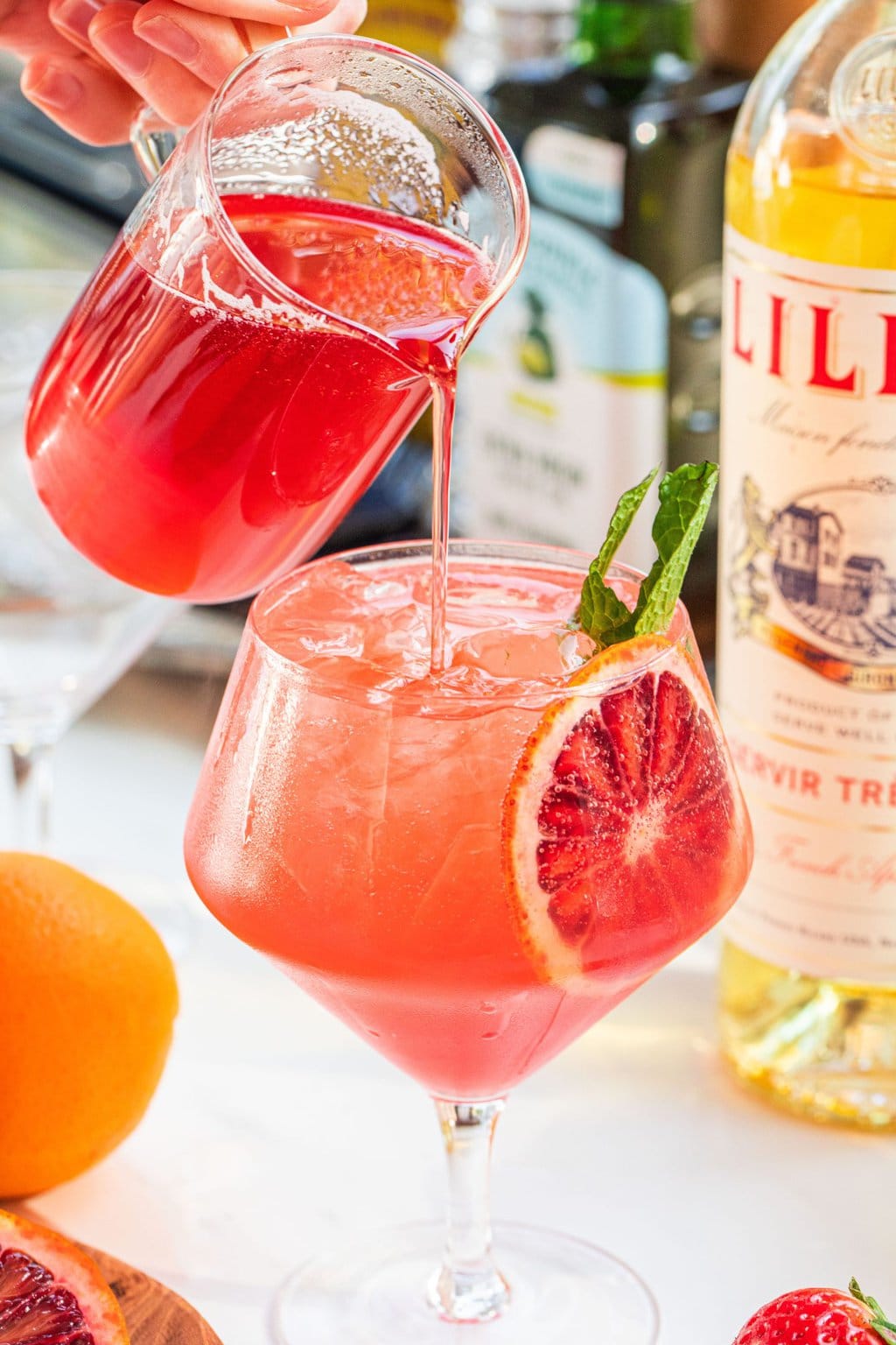 strawberry simple syrup being poured into a strawberry orange spritz cocktail garnished with an orange slice