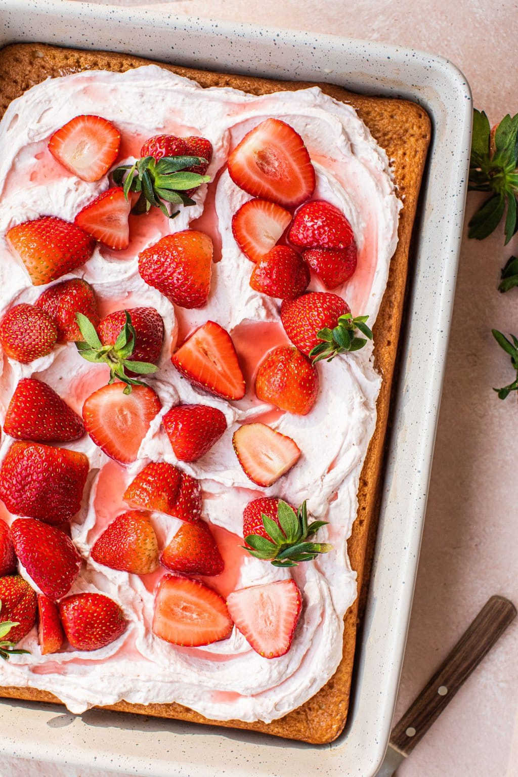 strawberry tres leches cake with light pink icing and fresh strawberries on the top