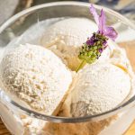 three dollops of lavender ice cream with honey in a bowl and a sprig of lavender garnishing the top