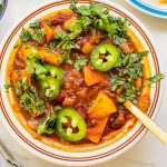 a bowl of veggie chili with jalapenos and herbs on top