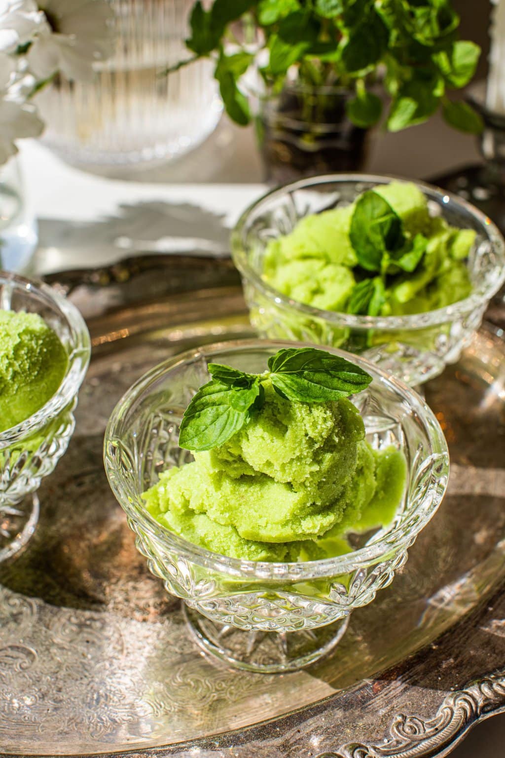 Three glasses of green pear sorbet on a silver serving dish garnished with mint leaves