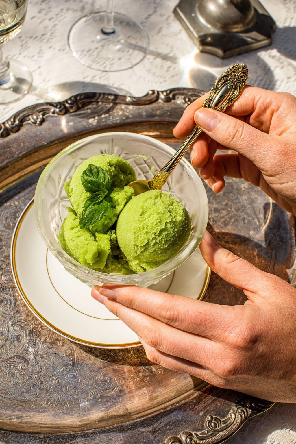 green sorbet in a glass dish on a silver platter with a spoon in it