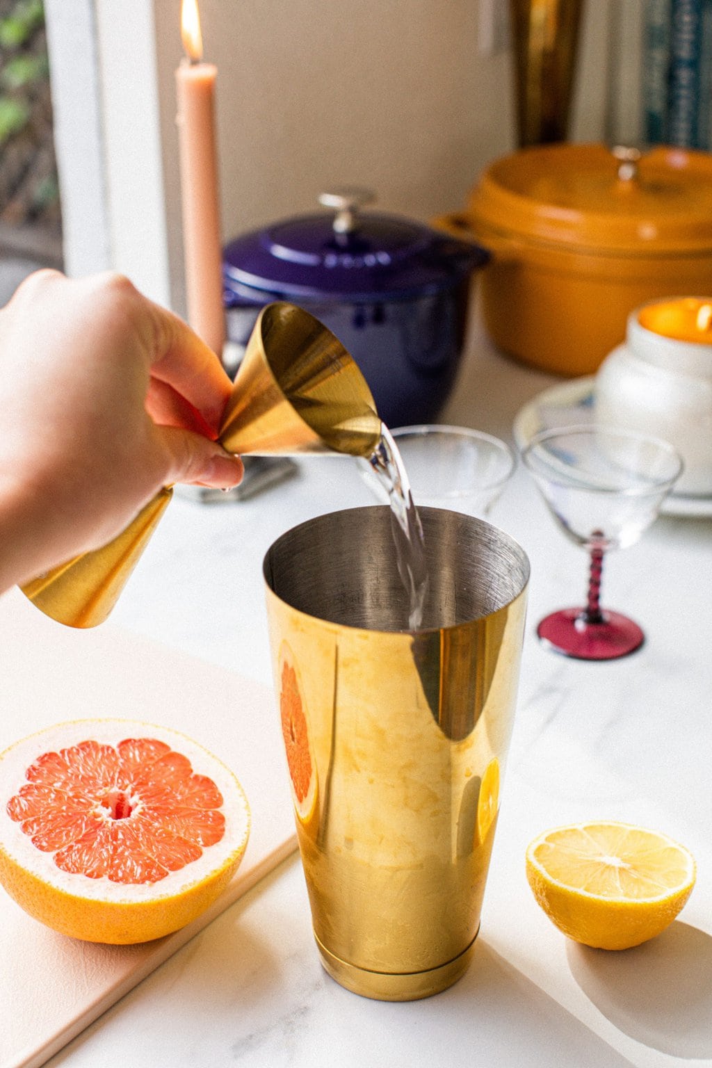 pouring alcohol into the golden cocktail shaker with slices of grapefruit and lemon to the sides