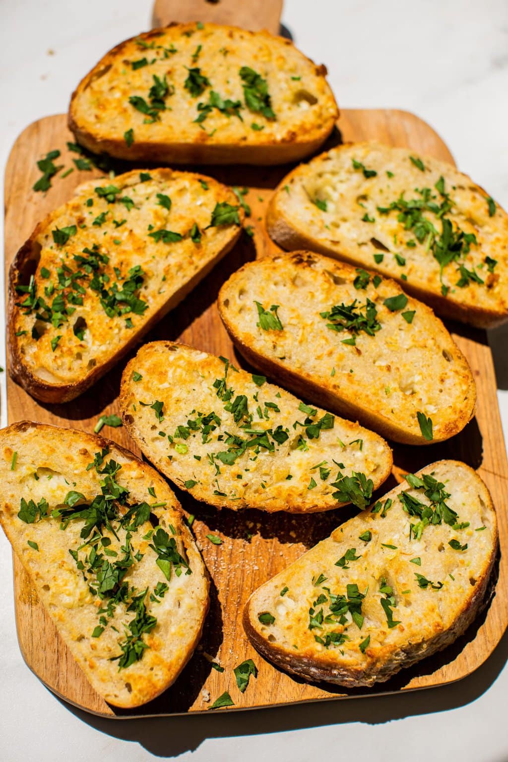 several slices of garlic bread topped with parsley on a wooden serving board