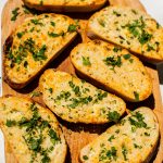 several slices of garlic bread topped with parsley on a wooden serving board