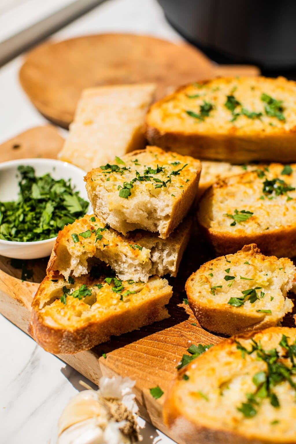 slices of garlic bread broken in half and with bites taken out of them topped with freshly chopped parsley on a wooden chopping board